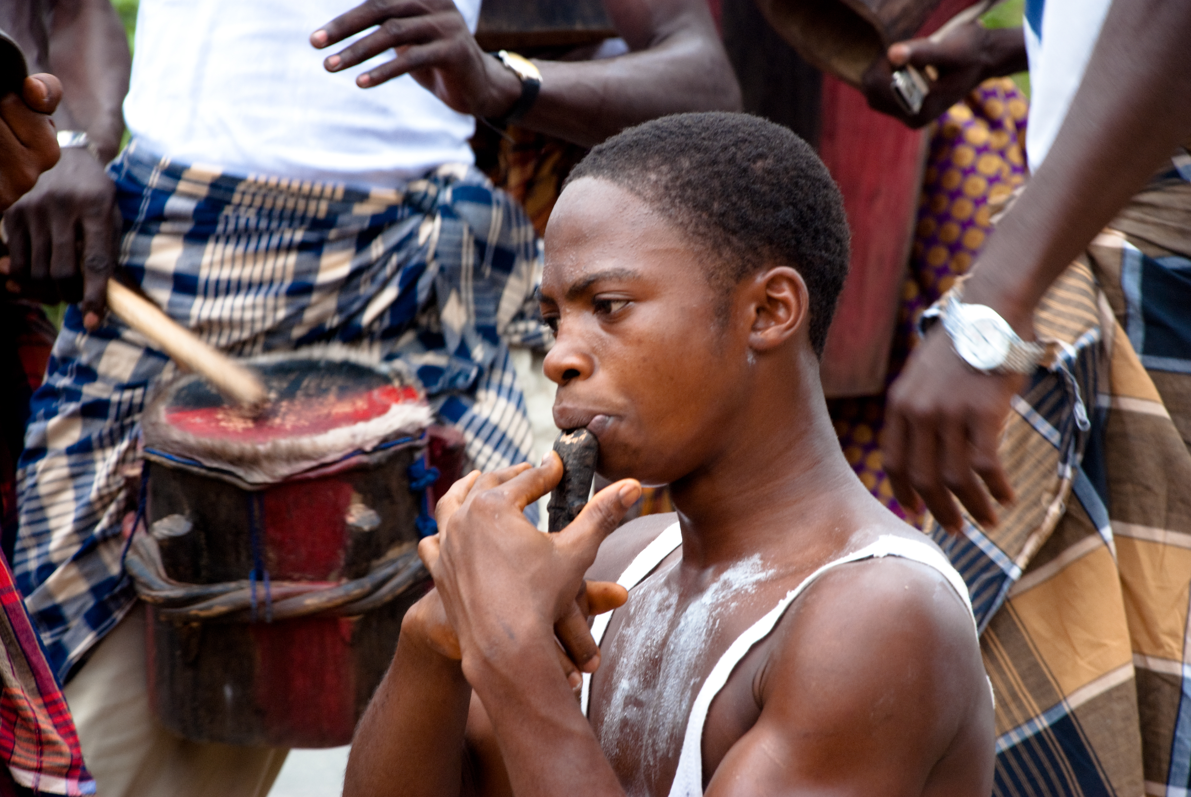 A close up portrait of a man playing a wooden flute with people in the backgroud.