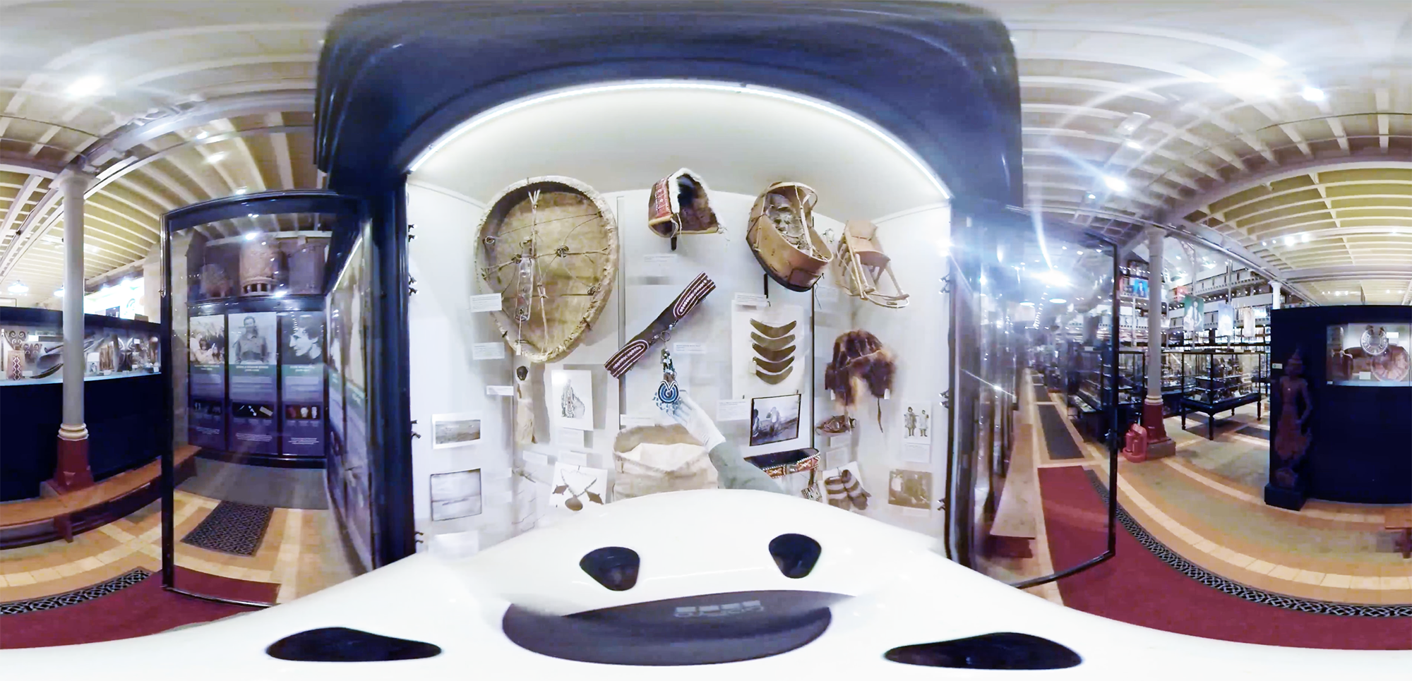 A 360 degree bodycam view focusing on a person's hand touching a blue beadwork object in the centre of an open display case.