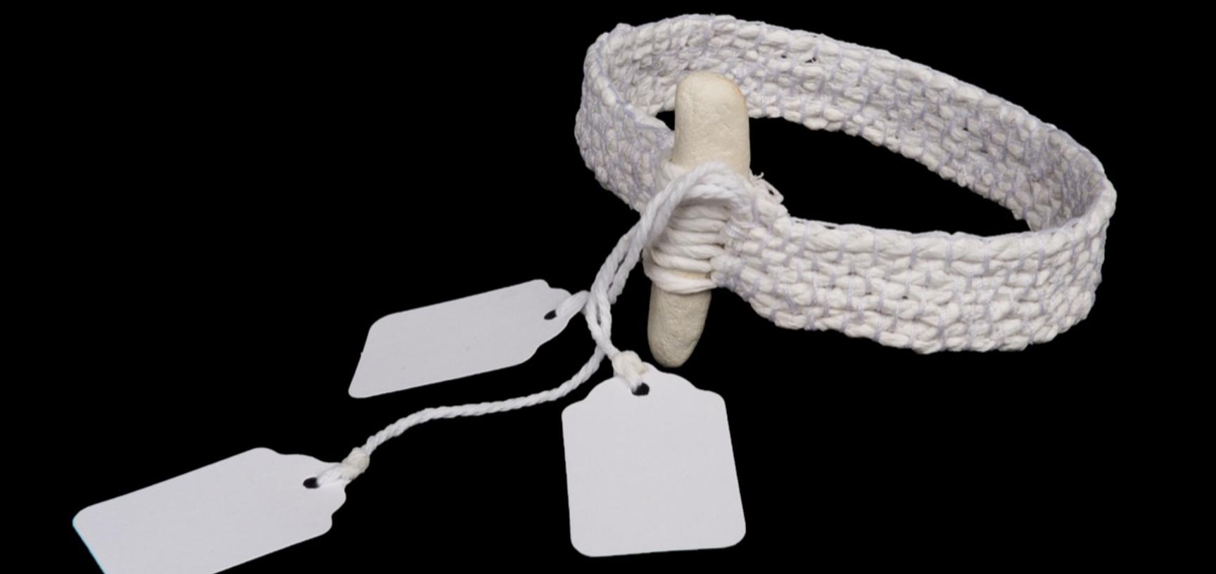 Arm band made from woven white material with small white parcel tags attached.