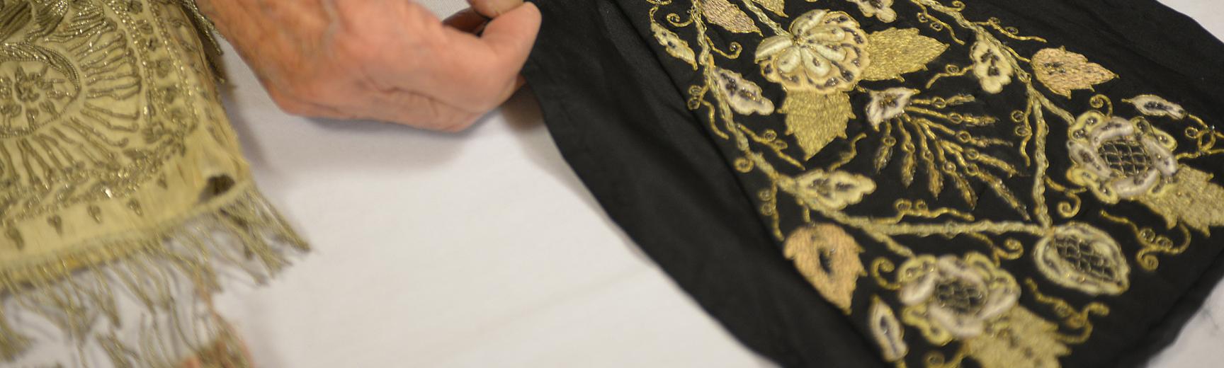 Hands holding a piece of black textile with golden embroidery