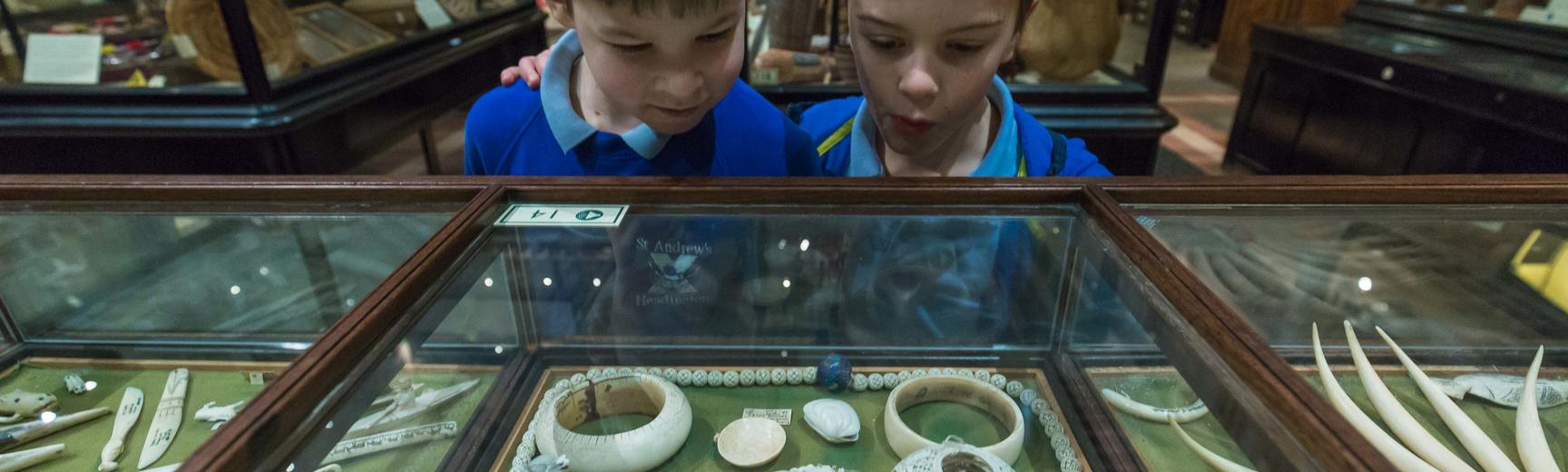 Two boys dressed in school uniform stare in wonder at objects intricately carved from ivory in the case in front of them.