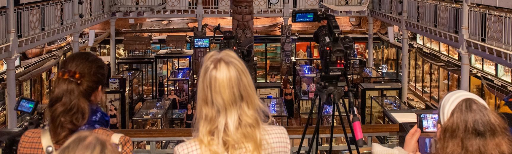 People watching a performance in the galleries with filming taking place via phones and a camera on a tripod