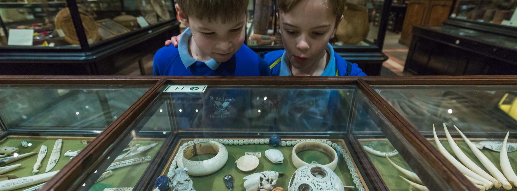 Two boys dressed in school uniform stare in wonder at objects intricately carved from ivory in the case in front of them.