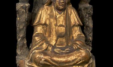 Wooden figure gilded in gold, seated under a bush.