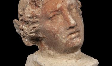 Very small statue of a head with Grecian-style hair.