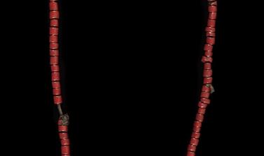 Necklace of red, white and blue beads attached to what looks like a brown leather string with a small amulet of the same material.