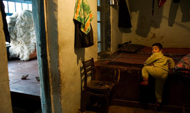 A boy climbing onto a platform in his home. Piles of locally grown cotton in the adjacent room will be used to make mattresses for a newly-wed couple. Karimov, Uzbekistan. Photograph by Carolyn Drake. March 2008.