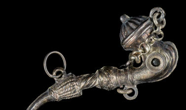 Silver pendant in the shape of a curved pipe with a small hole containing a lens at one end.  