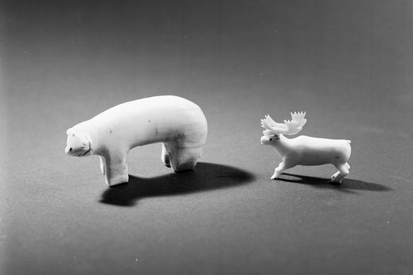 Small carved figure of a polar bear standing on four paws and looking to one side placed to the left of a caribou figure also standing on four legs and facing forwards with a fine set of antlers.