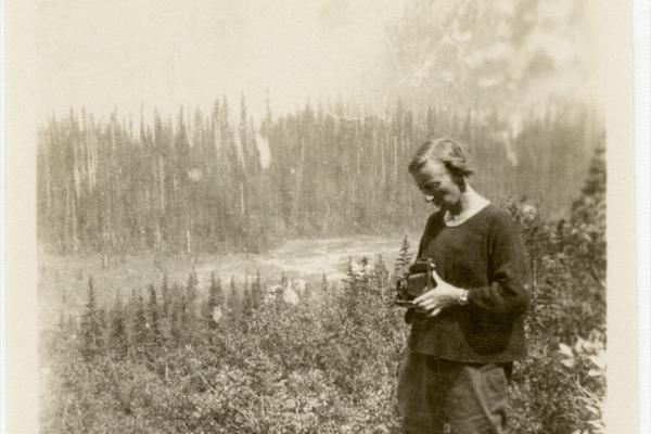 Old photo of a woman taking a photo of a wooded landscape