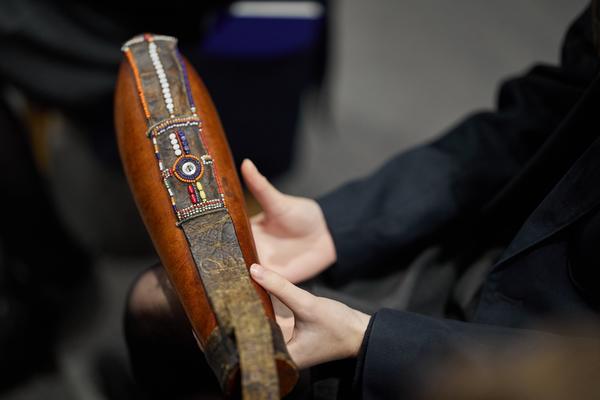 Close up of hands holding a gourd decorated with a beaded leather strap