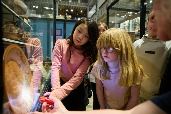 School children looking at case display with objects lit up by torchlight