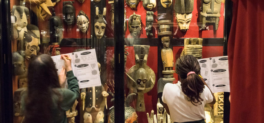 Two pupils stand in front of a glass case full of West African masks.