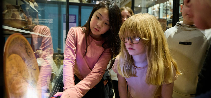 School children looking at case display with objects lit up by torchlight