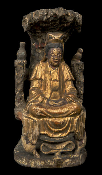 A gold wooden figure seated in a grand chair under a bush.  