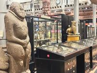 Carved stone figure alongside dark wooden display cases in the museum galleries