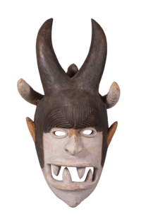 Wooden mask with a face featuring an open mouth with sharp teeth and horns on the top of the head.